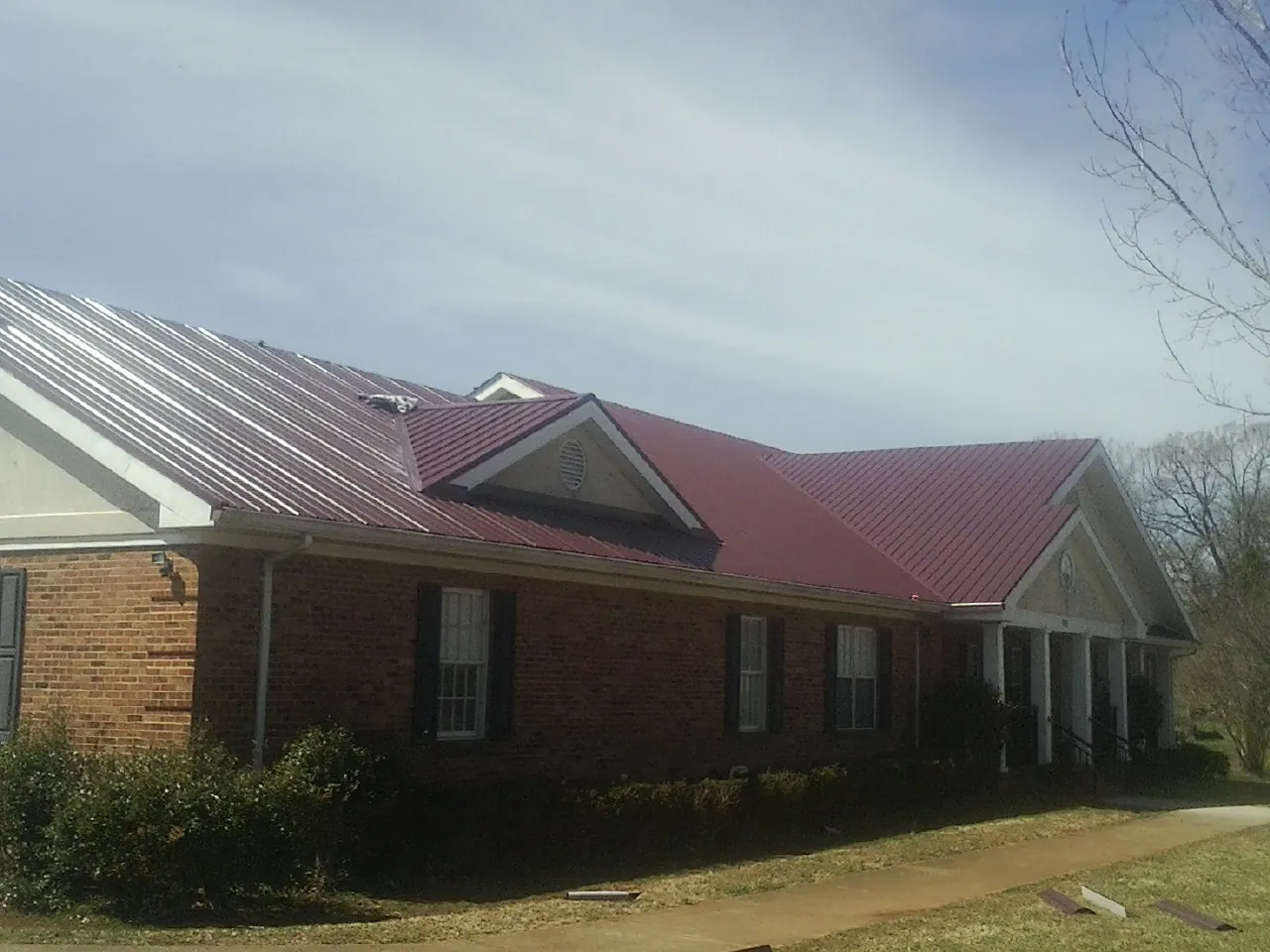 Red metal roof with gabled entries on a long brick building, from a Hail Damage Roof Repair job in Rifton