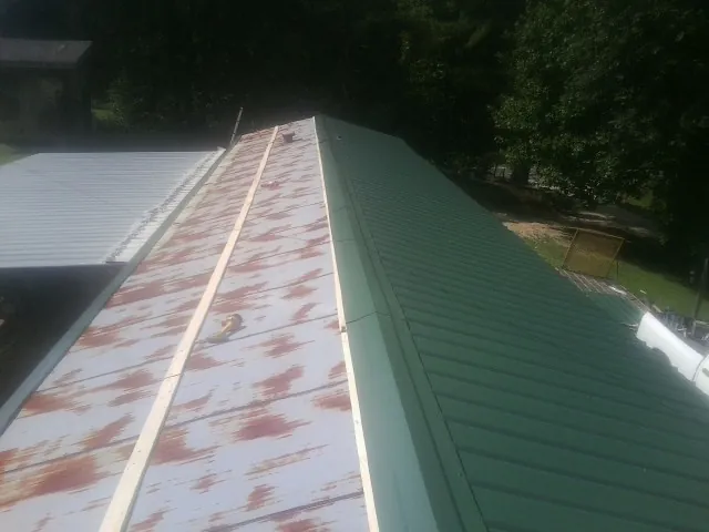 Old rusted panels beside newly installed green metal roofing — Wind Damage Roof Repair by Roofing Brothers in Rifton