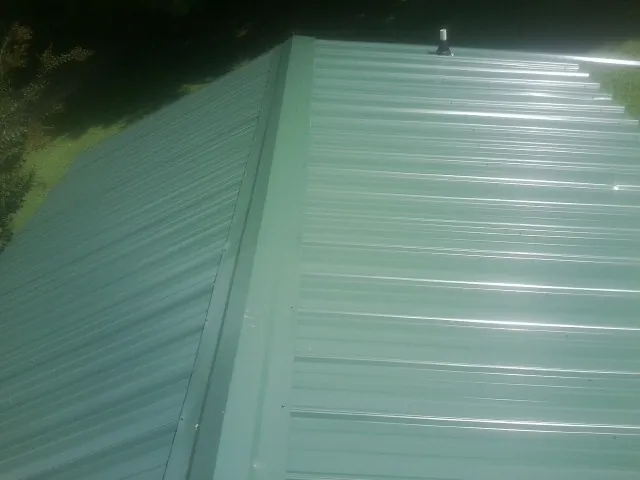 New green metal panels meeting at the ridge of a roof — Flat Roof Repair work by our crew in Rifton