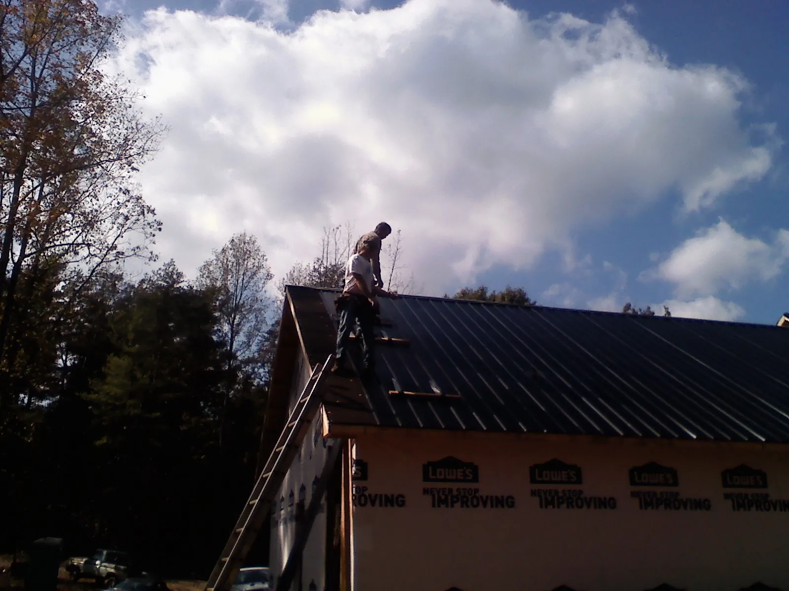 Roofer fastening dark metal panels high against a cloudy sky, from a Roof Inspection job in Rifton