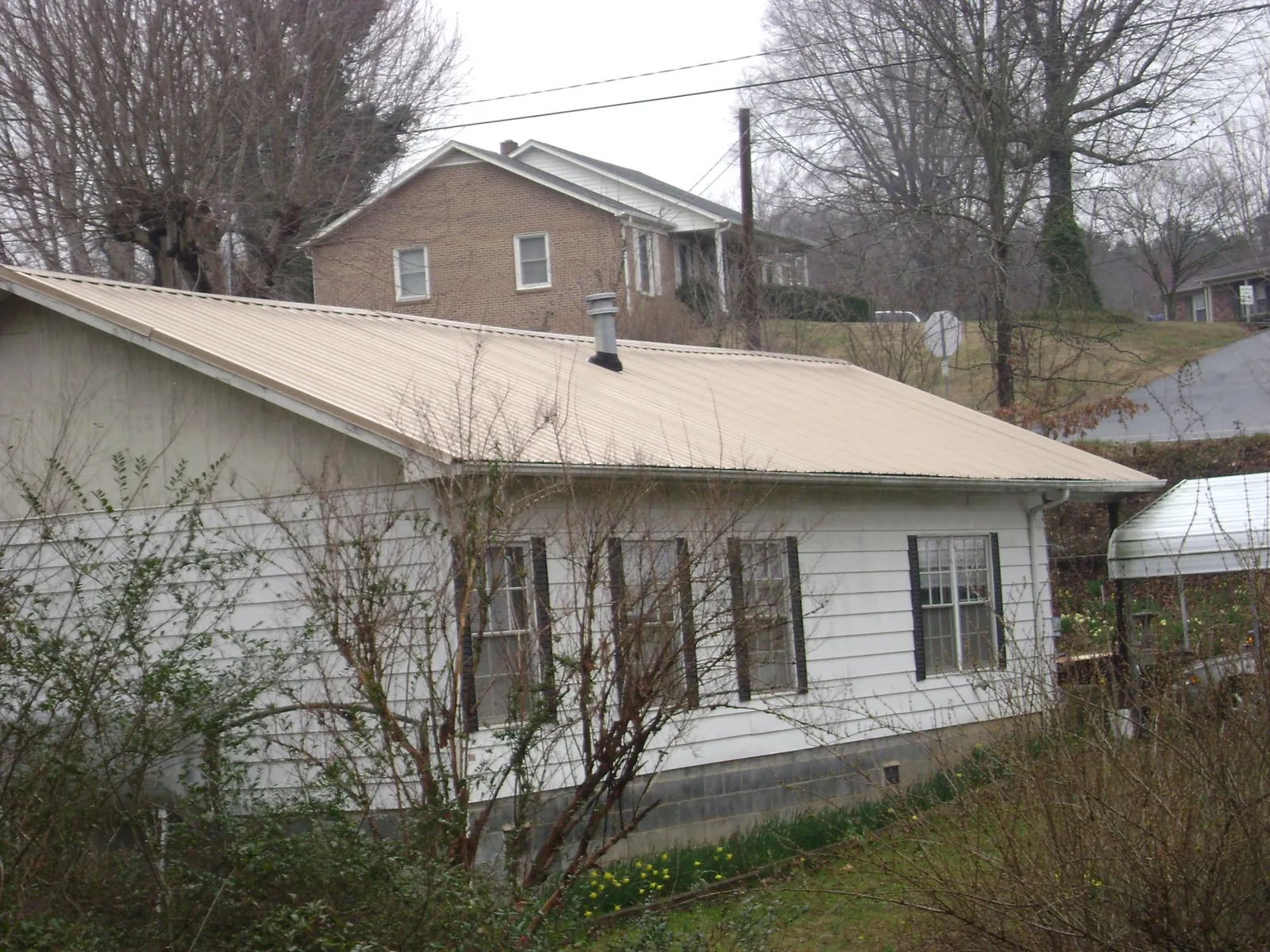 Tan metal roof on a white sided house set into a hillside — Commercial Roofing by Roofing Brothers in Rifton
